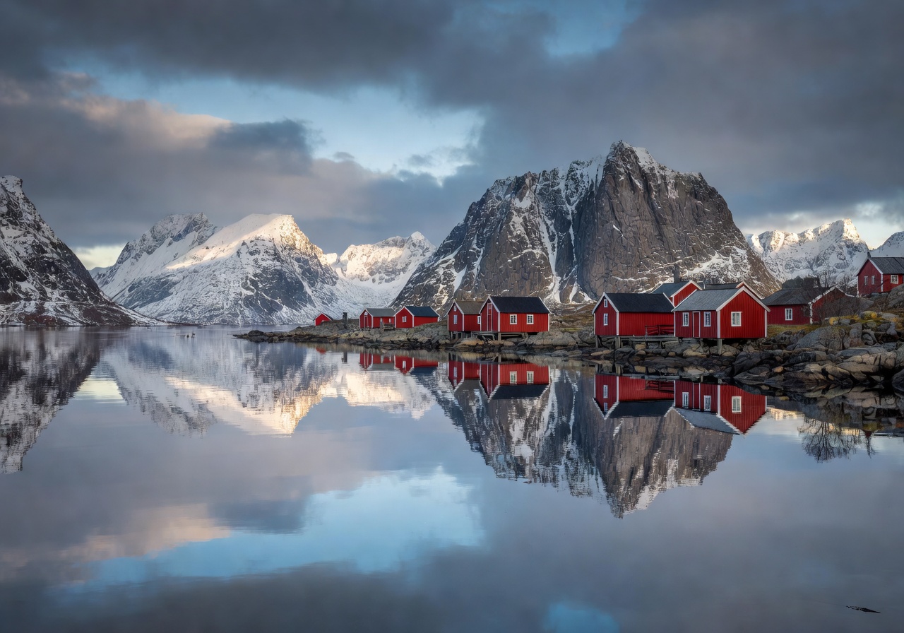 Lofoten Islands red fishing cabins reflected in calm Arctic waters with dramatic peaks behind